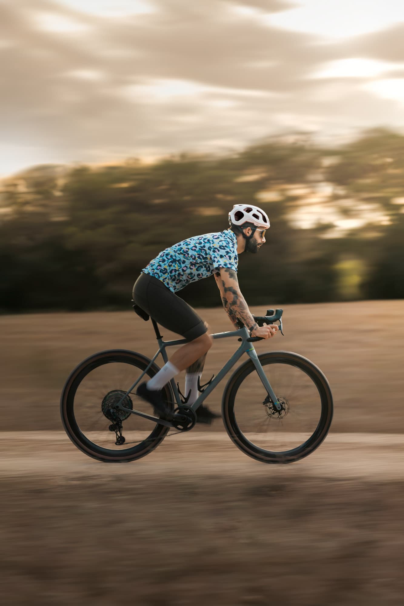 A male rider in a blue leopard-spot Pamera shirt blurs past in the late golden light.