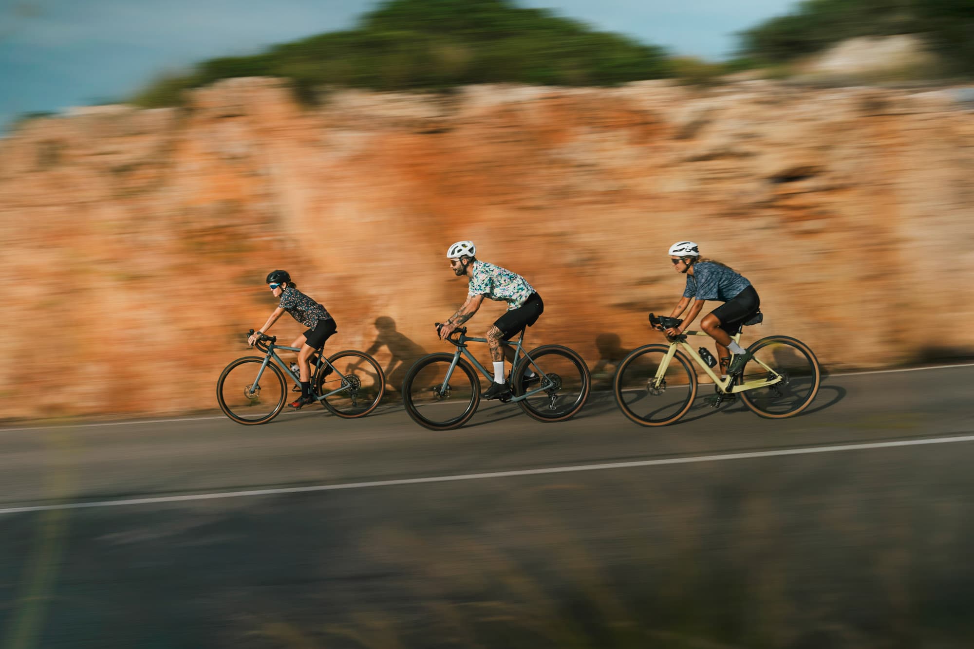 Three Pamera riders sweeping past a rust-orange rock wall in motion blur.