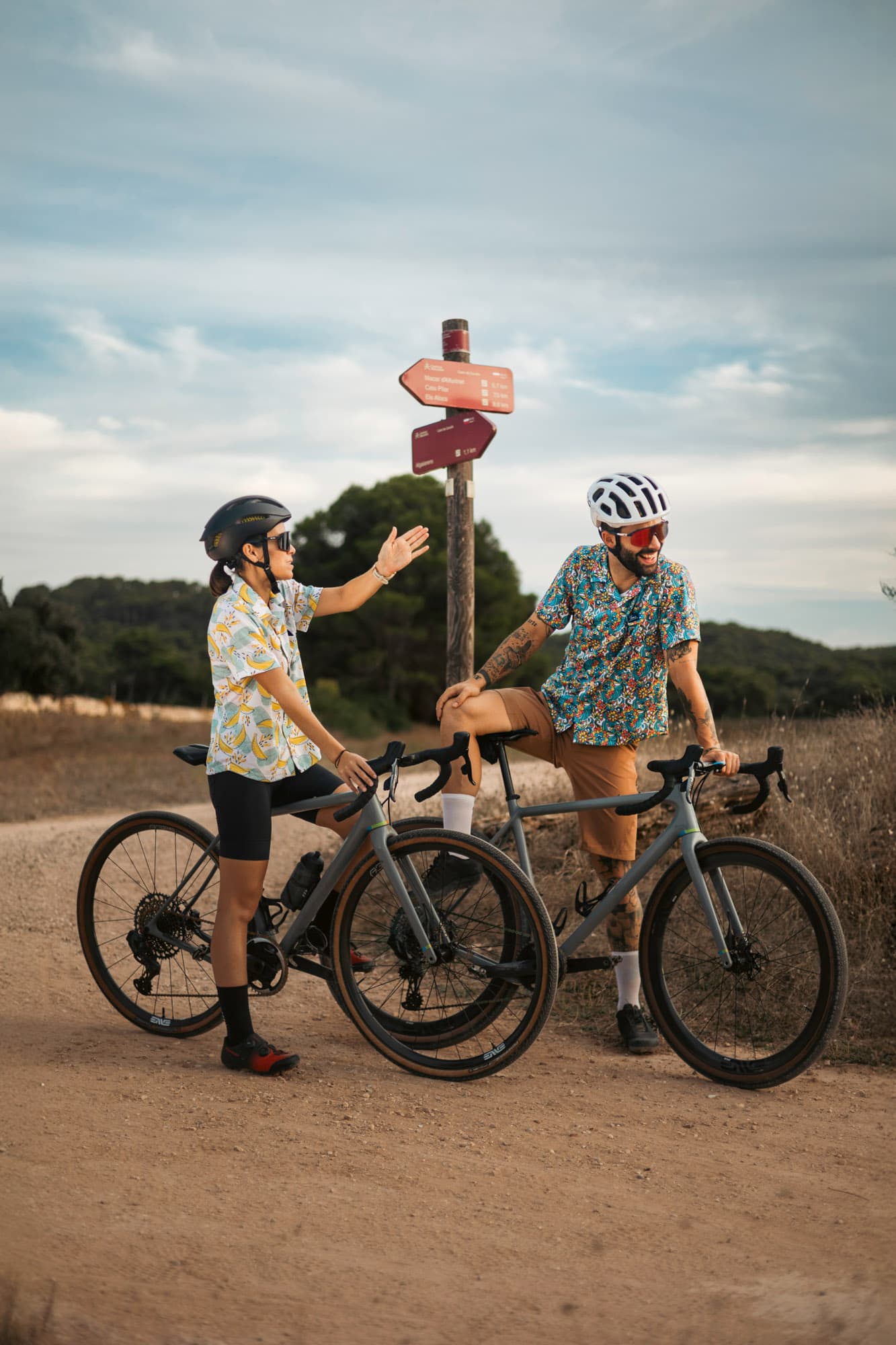 A couple paused at a wooden trail signpost, mid-conversation in bright Pamera shirts.