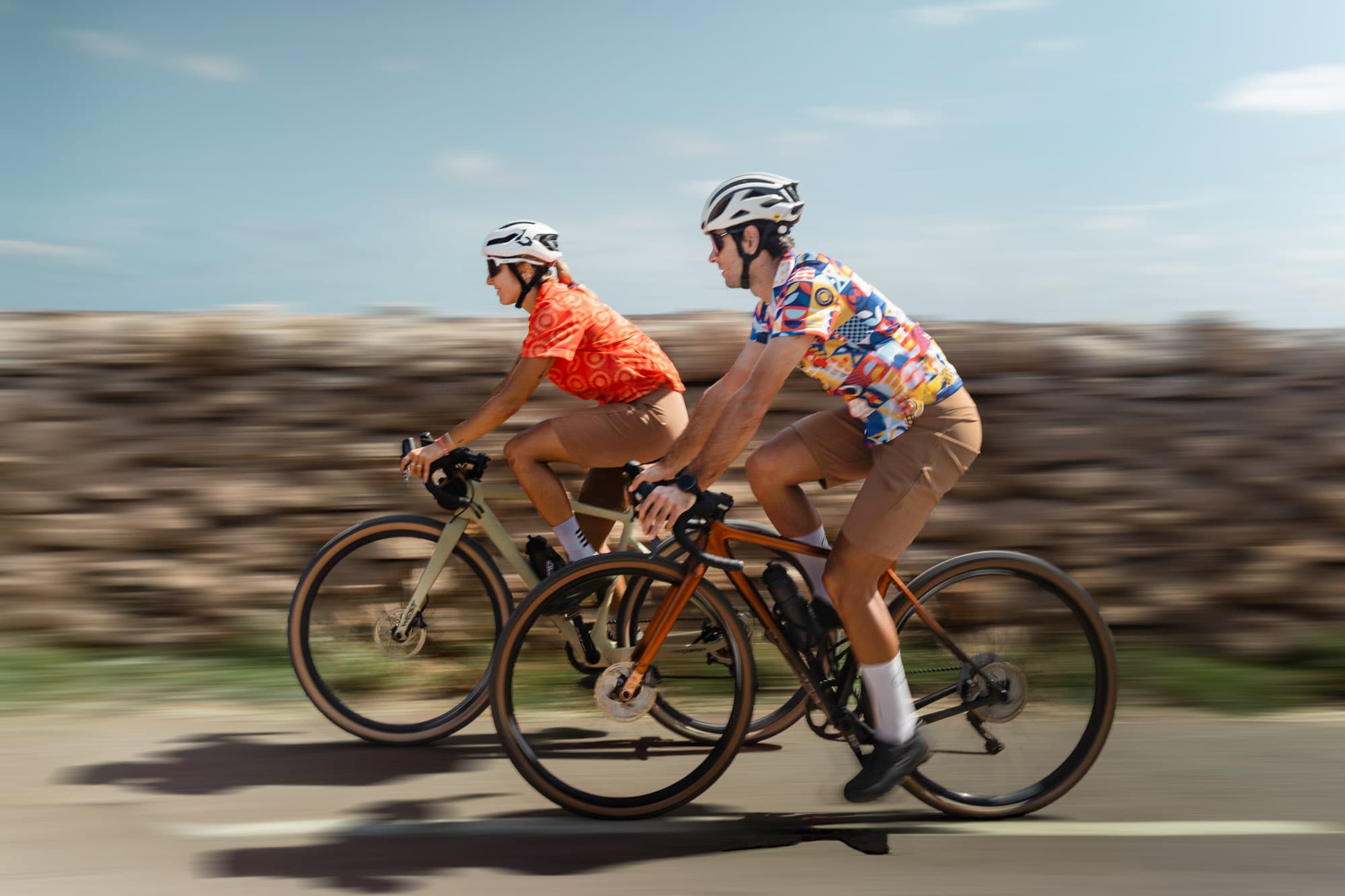 Two Pamera riders in profile blur past a low stone wall at speed.