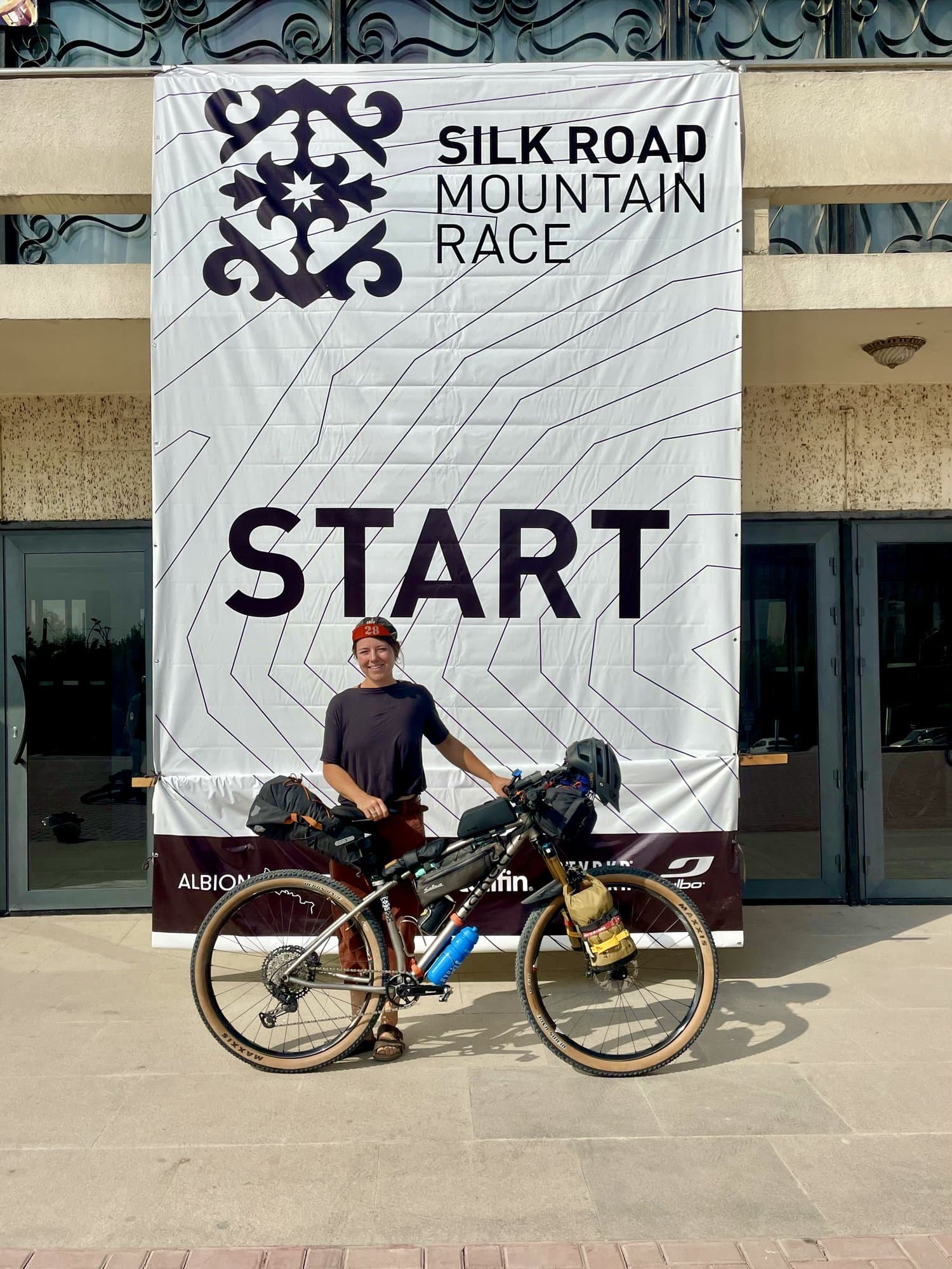 Britt Shalagan with her loaded Naked titanium hardtail under the Silk Road Mountain Race start banner.