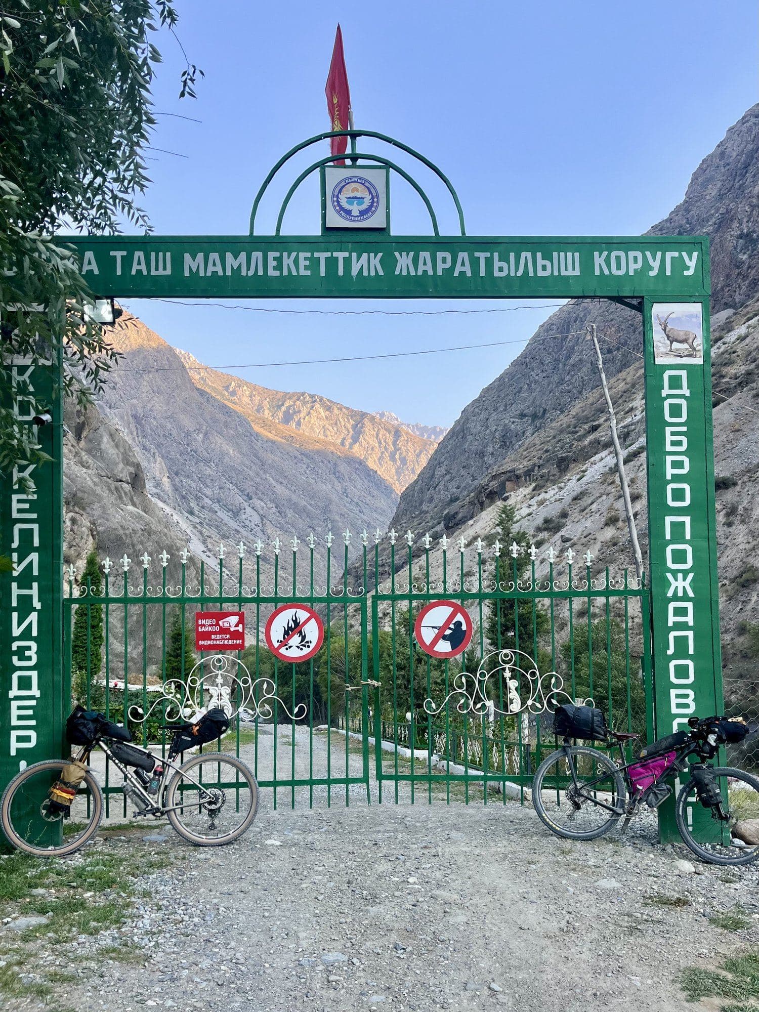 Two loaded bikepacking rigs at the green entrance gate of a state nature reserve in Kyrgyzstan.
