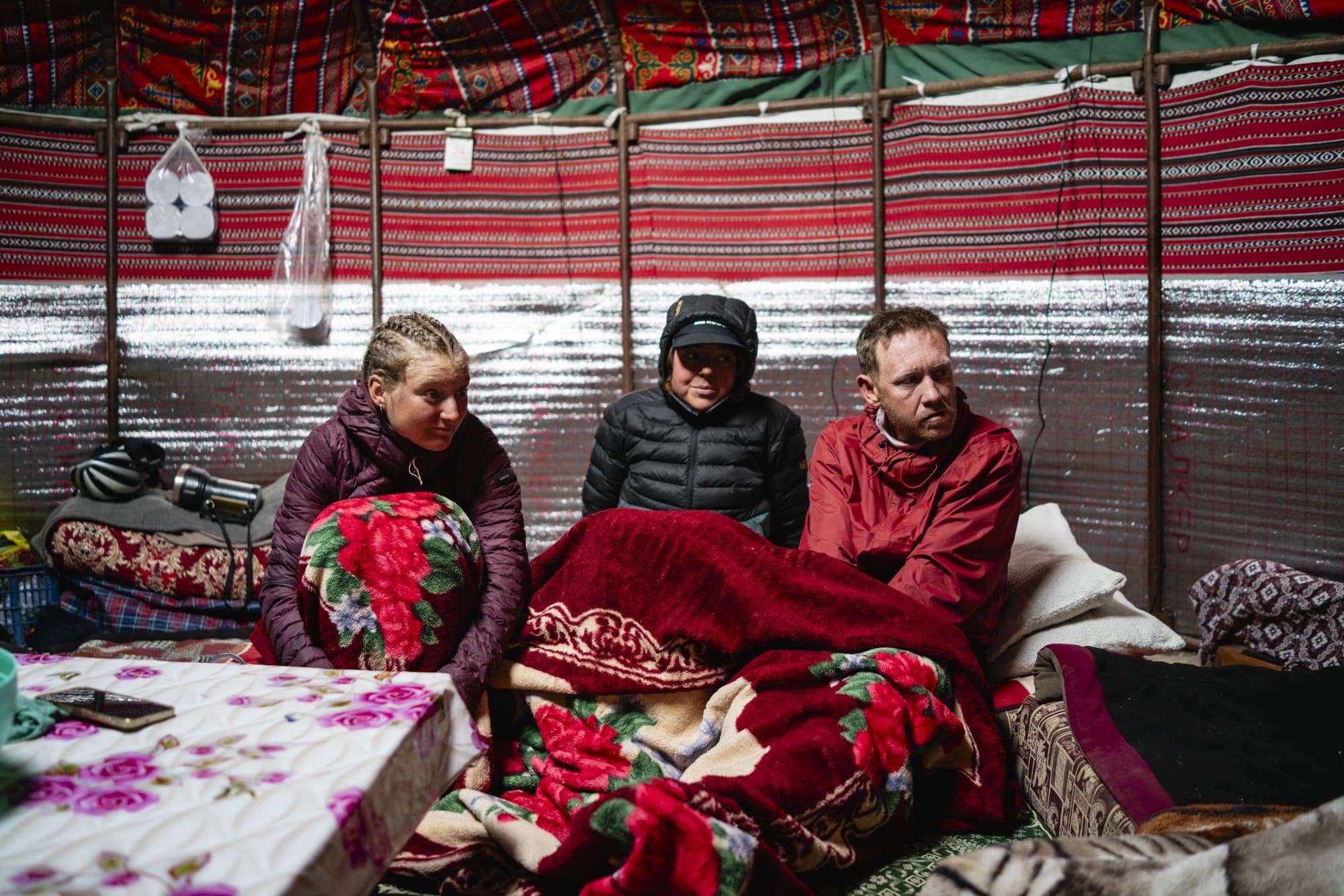 Three racers wrapped in red blankets inside a yurt.